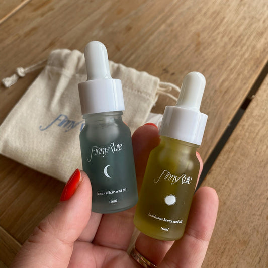 Two small bottles with droppers labeled 'Finny Rue' held in a hand on a wooden surface.